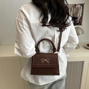 Minimalist brown faux leather crossbody bag with golden bow hardware worn by a model