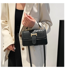 Close-up of black woven square bag featuring a gold H-buckle and textured flap detail