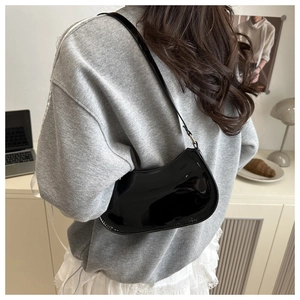 Detail of a black patent leather crescent hobo bag worn over the shoulder in a minimalist style