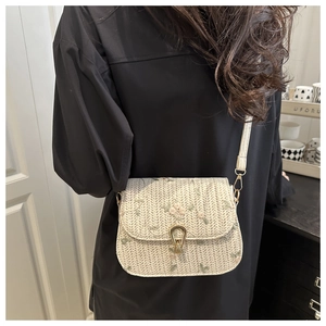 Detail of beige woven saddle bag with floral embroidery and golden metal clasp lock