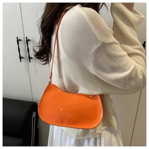 Detail of orange patent leather shoulder bag with glossy finish on cream knit top