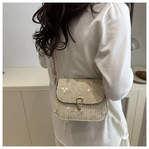Detail of summer straw saddle bag with pink floral embroidery and metal buckle closure
