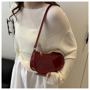 Detail of a dark red patent leather crescent shoulder bag with gold metal zipper