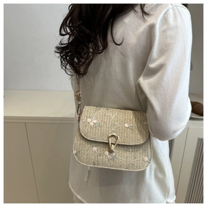 Detail of hand-woven straw bag featuring delicate pink flower embroidery and golden clasp