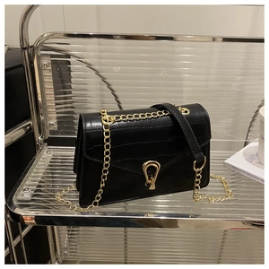 Detail view of black crocodile pattern leather bag with golden U-shaped buckle and chain strap
