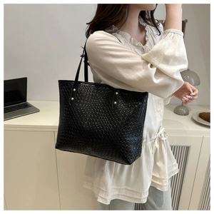 Detail view of woven tote bag with leather handles and gold rivet accents on the side