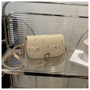 Close-up of straw woven crossbody bag with floral embroidery and golden horseshoe buckle