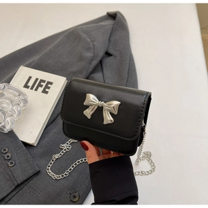 Detail of a black leather mini crossbody bag featuring a silver bow buckle and chain strap