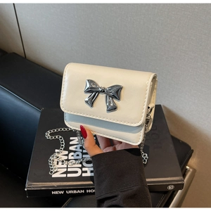 Detail of a creamy white crossbody bag with a large metallic silver bow and chain strap