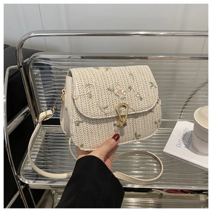 Detailed close-up of straw woven crossbody bag with delicate floral embroidery and gold lock