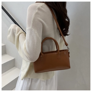 Détail d'un sac à bandoulière marron avec logo FASHION embossé sur un escalier blanc