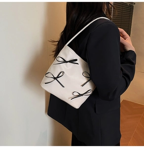 Close-up of cream PU shoulder bag featuring black bows on a model wearing a black blazer