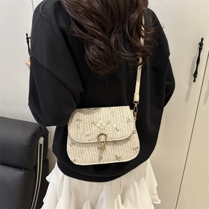 Fashionable woven straw crossbody bag with floral pattern and golden heart clasp on model