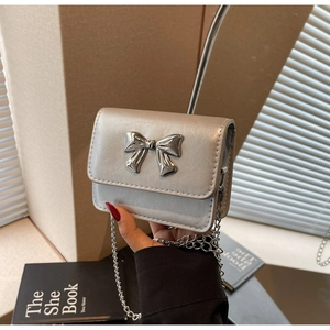 Detail of silver crossbody bag featuring a metallic bow and elegant chain strap