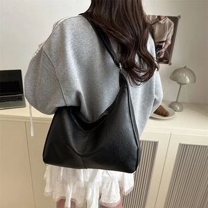 Large black textured leather tote bag worn by a model in a minimalist home setting
