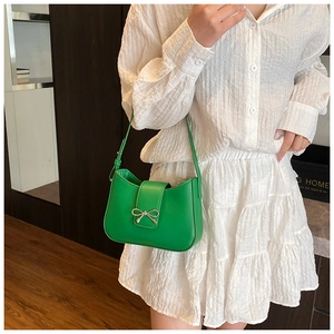 Close-up of green crescent shoulder bag with silver bow detail worn with a white shirt