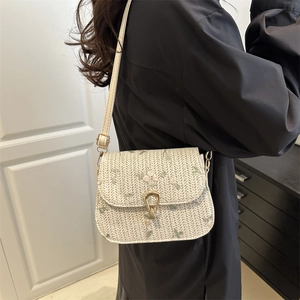 Straw crossbody bag with floral embroidery and gold horseshoe buckle in a modern setting