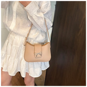 Detail of minimalist beige crescent shoulder bag with silver bow ornament on white dress