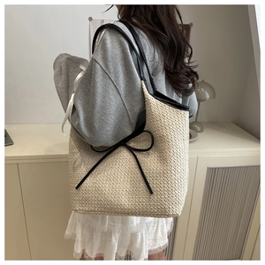 Close-up of woven cream tote bag featuring a decorative black leather bow detail