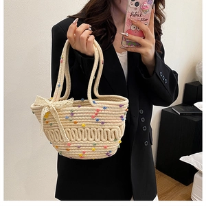 Close-up of cream woven bucket bag with colorful pom-poms and a delicate lace bow