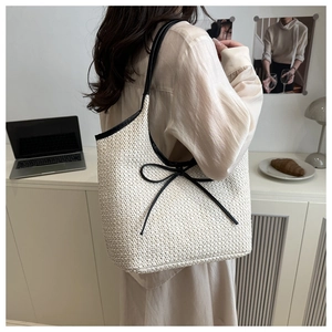 Detail view of a cream woven tote bag with black trim and a delicate bow accent