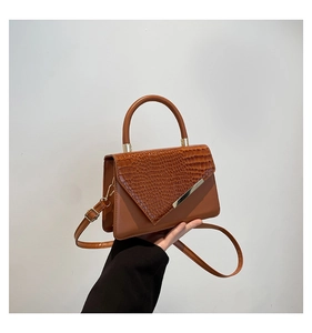 Detail of brown faux leather handbag with crocodile pattern flap and metal trim