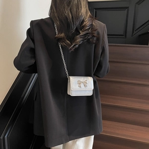 Chic silver crossbody chain bag with a metallic bow clasp shown on a shoulder