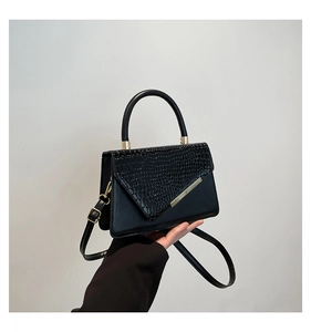 Detail of black leather square bag with crocodile pattern texture and gold hardware