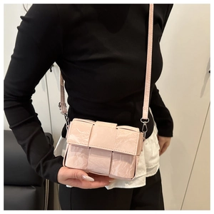 Detail of light pink woven crossbody bag featuring glossy synthetic leather and silver hardware