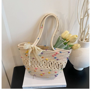 Detail of handmade woven bucket bag with colorful pom poms and a delicate lace bow accent