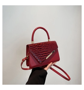 Detail of red crossbody bag featuring crocodile texture and V-shaped gold hardware