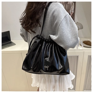 Detail of a black glossy pleated bucket bag with a small silver bow decoration