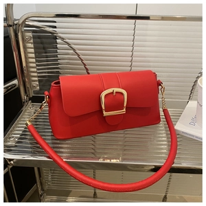 Dettaglio di una borsa a spalla rosso acceso in pelle con grande fibbia dorata su ripiano