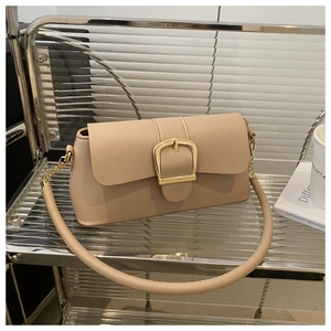Dettaglio della borsa a tracolla beige con grande fibbia dorata su uno scaffale moderno