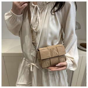 Detail of beige woven crossbody bag featuring unique wrinkled paper texture and metal buckle