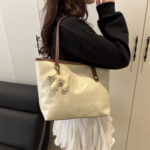 Creamy white large tote bag with brown trim and puppy charm worn by a model