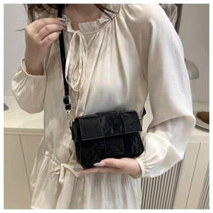 Close-up of black woven leather shoulder bag with textured pleats and silver metal buckle