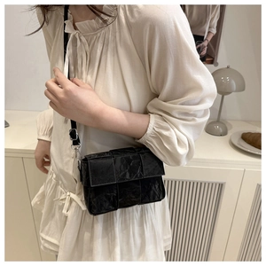 Close-up of black pleated textured square bag with silver metal buckle on leather strap