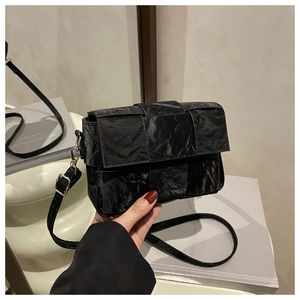 Detail of the black pleated crossbody bag with a modern woven-style flap and silver buckle