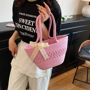 Pink woven straw bucket bag with white lace bow held by a model in a casual setting