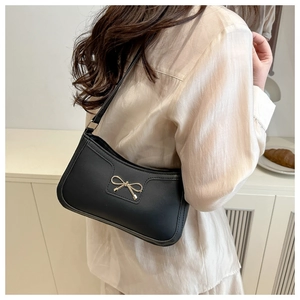Detail of a black crescent armpit bag featuring a gold bow buckle on a beige shirt