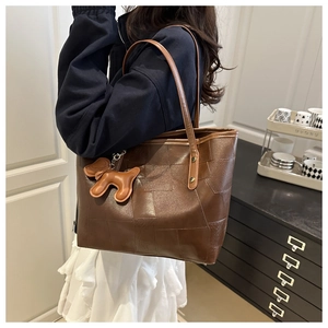 Detail view of brown vintage tote bag with contrast panels and cute puppy charm accessory