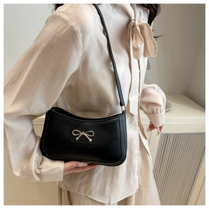 Detail of black leather crescent bag with golden bow clasp shown on a model's shoulder