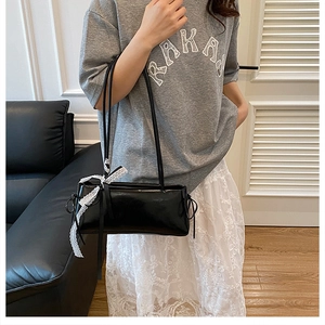 Detalle de bolso baguette de cuero negro con lazos de encaje blanco y cordones laterales