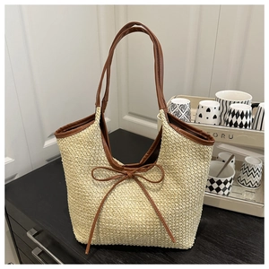 Detail view of straw tote bag with brown leather handles and a decorative bow tie
