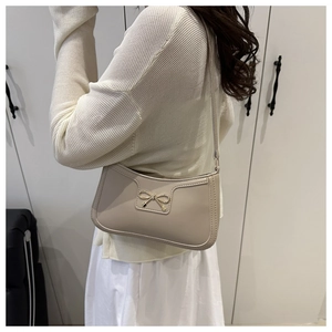 Detail of cream crescent hobo bag with gold bow clasp worn as an underarm shoulder bag