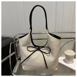 Close-up of woven tote bag featuring black leather trim and a decorative ribbon bow
