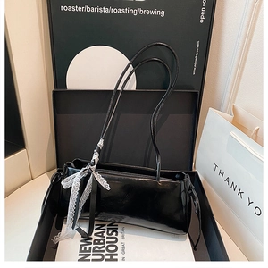 Detalle de bolso baguette en charol negro con lazo de encaje blanco y acabado brillante