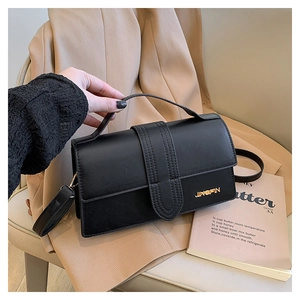 Détail d'un sac à main en cuir noir avec logo en métal doré sur un blazer beige en fond