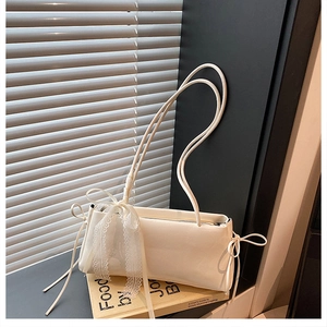 Detalle de bolso de hombro blanco crema con cinta de encaje y lazo sobre libros
